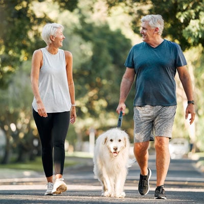 mature-couple-walking-a-dog-and-looking-at-eachother-in-a-park-400x400
