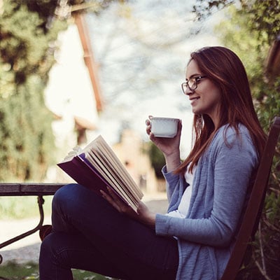 profile-shot-of-a-woman-drinking-coffee-and-reading-in-an-outdoor-park-like-setting-400x400